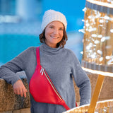 Woman wearing a gray sweater and white beanie with a red bag, standing in front of festive lights.