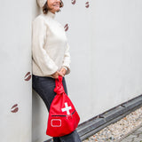 Person holding a red bag with a white cross against a light-colored wall.