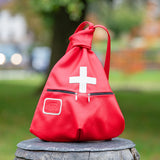 Red backpack with a white cross on a wooden stump in a park setting