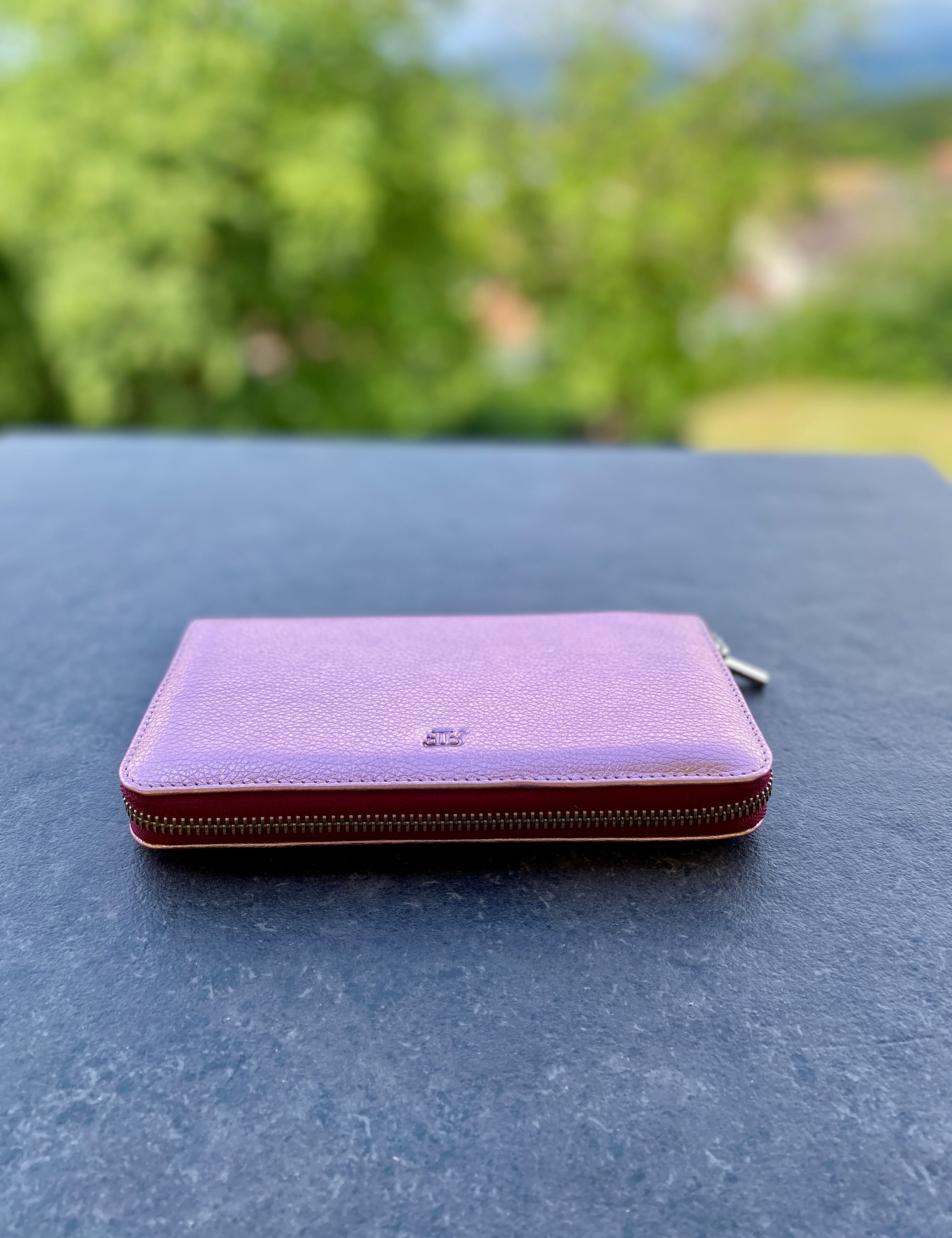 Purple wallet on a dark surface with a blurred green outdoor background